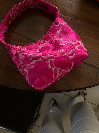 A bright pink shoulder bag with floral embroidery on a dusty pink canvas
