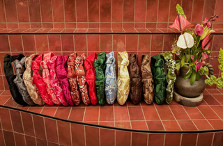 Colorful fabric samples arranged on a shelf with a vase of flowers in the background. Nudo Mini Bags